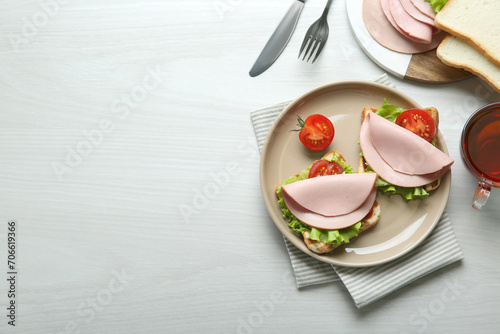Plate of tasty sandwiches with boiled sausage, tomato and lettuce on white wooden table, flat lay. Space for text