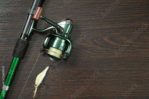 Fishing rod with reel and lure on dark wooden background, top view. Space for text
