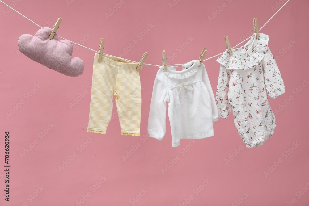 Different baby clothes and cloud shaped pillow drying on laundry line against pink background Different baby clothes and cloud shaped pillow drying on laundry line against pink background