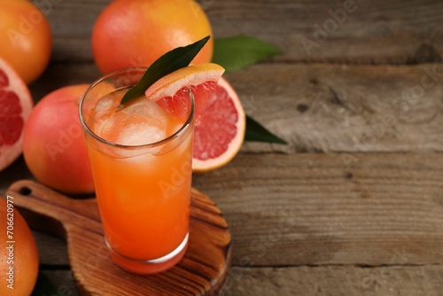 Tasty grapefruit drink with ice in glass and fresh fruits on wooden table. Space for text