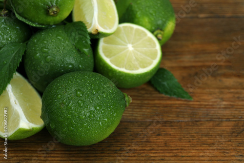 Pile of fresh wet limes and leaves on wooden table, closeup. Space for text