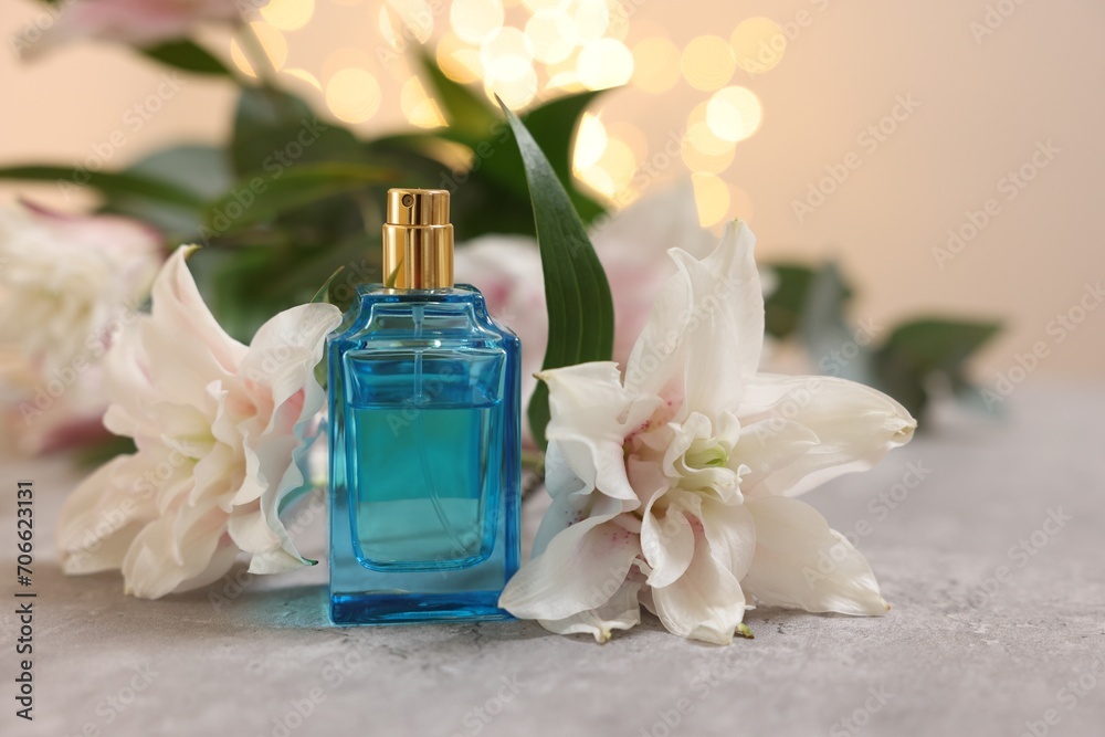 Bottle of perfume and beautiful lily flowers on table against beige background with blurred lights, closeup Bottle of perfume and beautiful lily flowers on table against beige background with blurred lights, closeup
