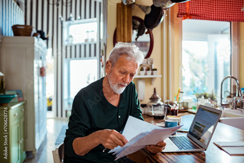 Senior man reading bill document at home kitchen photo