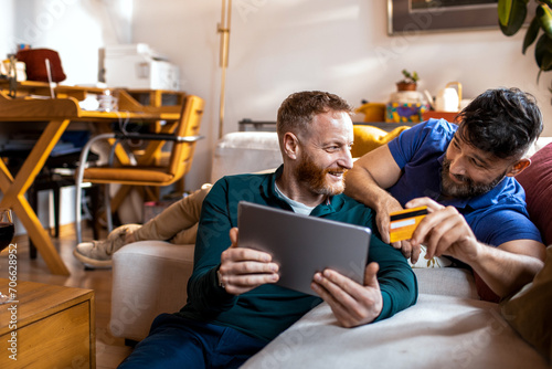 Gay couple shopping online at home with credit card and tablet photo