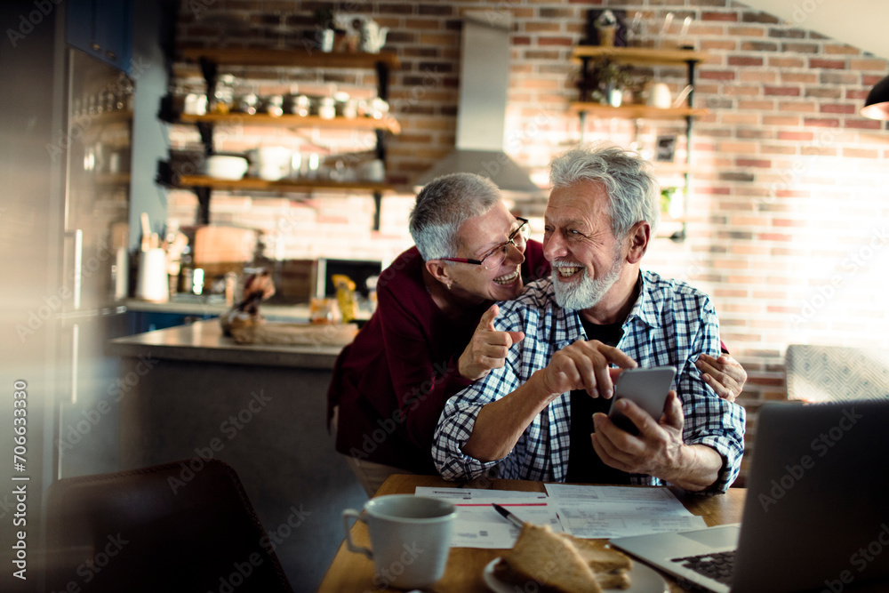 Senior Couple Laughing and Looking at Smartphone in home