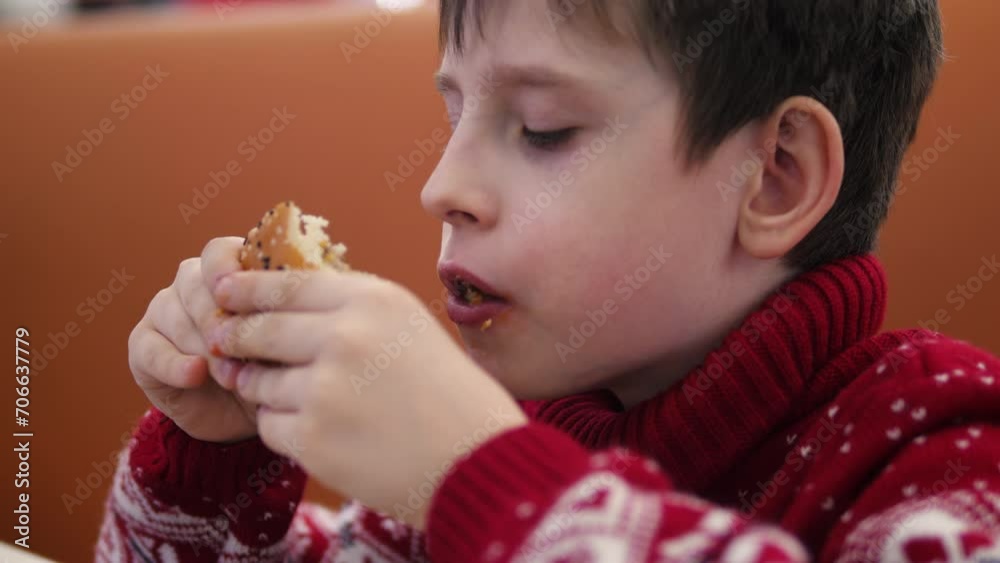 hungry Caucasian schoolboy 9 years old eats a cheeseburger in a cafe. teenager eats fast food. junk food concept hungry Caucasian schoolboy 9 years old eats a cheeseburger in a cafe. teenager eats fast food. junk food concept