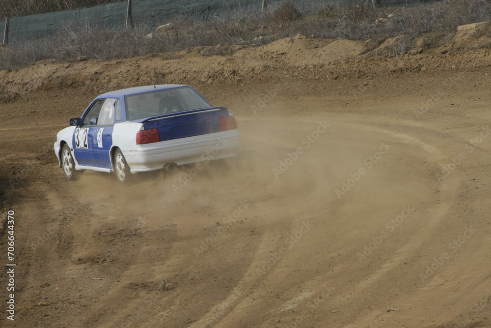 Classic cars gracefully drift around a rally track, swirling dust in a captivating display of vintage speed.