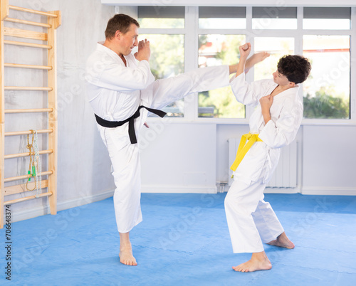 Dynamic underage boy and middle-aged man performing karate techniques in pair during workout session