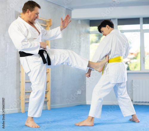 Dynamic underage boy and middle-aged man performing karate techniques in pair during workout session