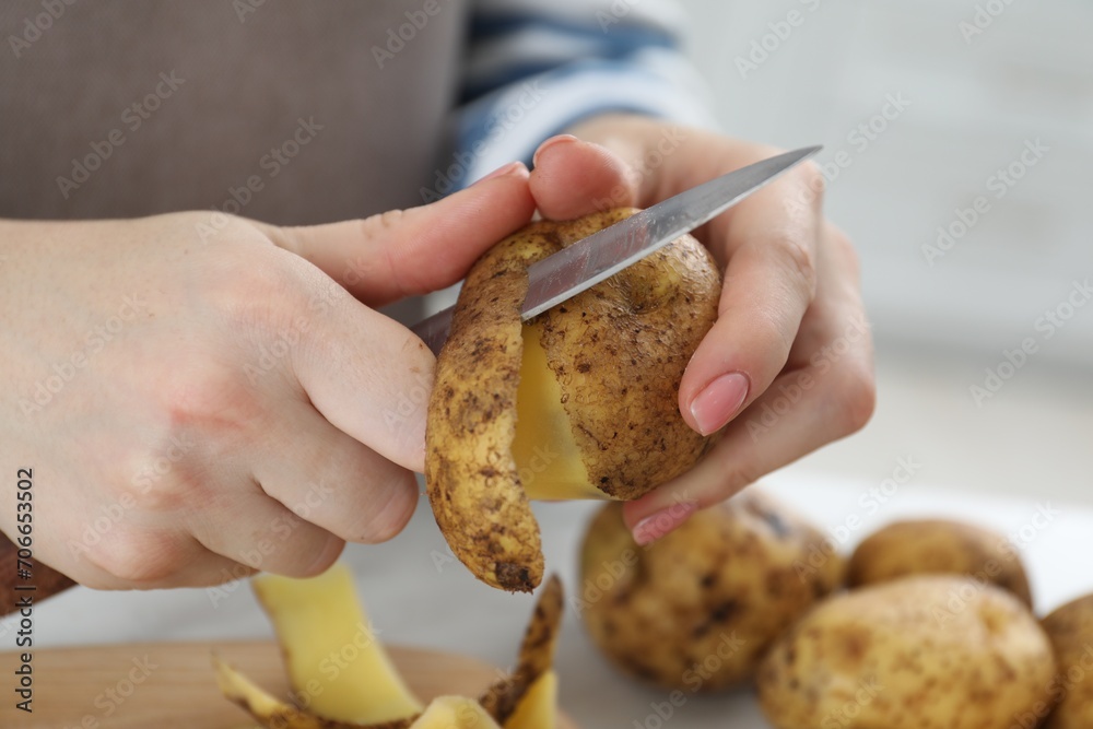 Woman peeling fresh potato with knife at table, closeup