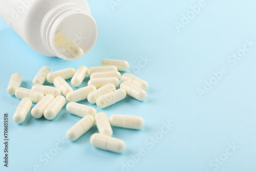 Bottle and vitamin capsules on light blue background, closeup. Space for text