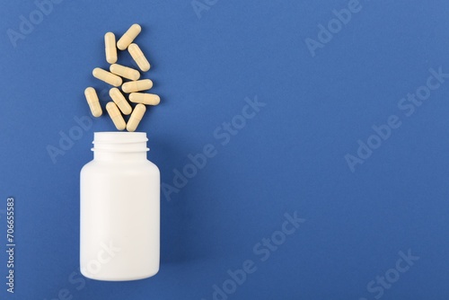 Bottle and vitamin capsules on blue background, top view. Space for text
