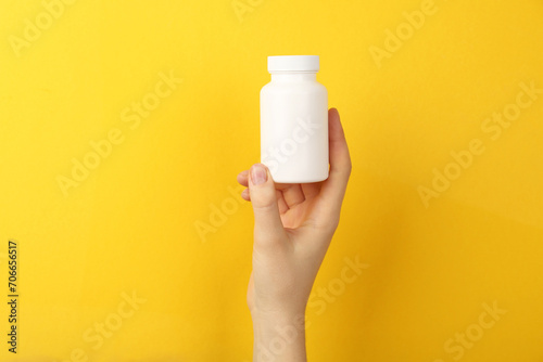 Woman holding blank white jar of vitamins on yellow background, closeup. Space for text photo