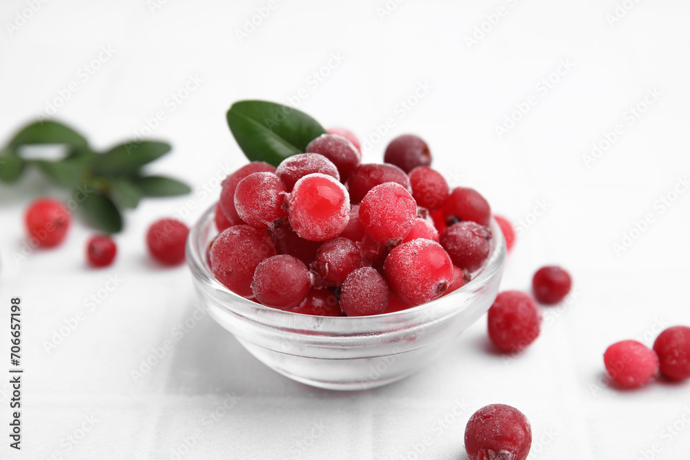 Frozen red cranberries in bowl and green leaves on white tiled table, closeup Frozen red cranberries in bowl and green leaves on white tiled table, closeup