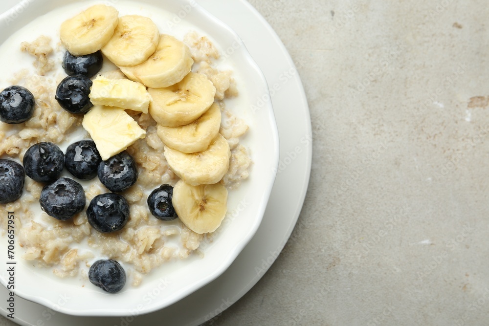 Tasty oatmeal with banana, blueberries, butter and milk served in bowl on light grey table, top view. Space for text Tasty oatmeal with banana, blueberries, butter and milk served in bowl on light grey table, top view. Space for text