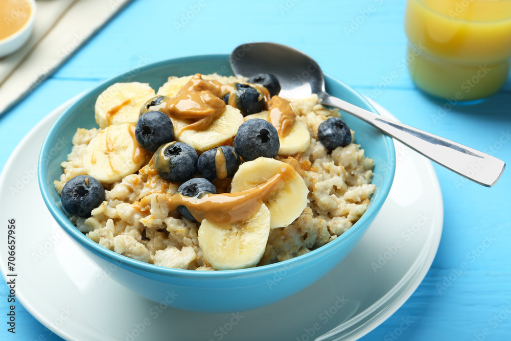 Tasty oatmeal with banana, blueberries and peanut butter served in bowl on light blue wooden table Tasty oatmeal with banana, blueberries and peanut butter served in bowl on light blue wooden table