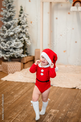 Cute baby toddler girl child in a red suit and santa hat during the Christmas holiday at home. Selective focus. The concept of New year and Christmas, the atmosphere of fun and comfort.