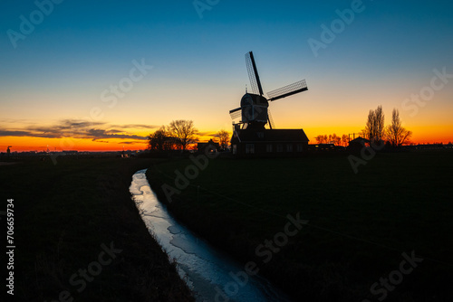 Silhouette of a traditional Dutch windmill against a colorful twilight sky