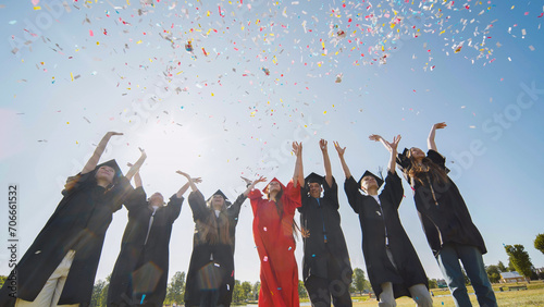 Happy college graduates throw colorful confetti against the rays of sunshine. photo
