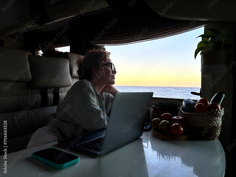 Fototapeta premium One modern adult woman digital nomad working on laptop sitting inside a motorhome camper van and using laptop computer with roaming traveler connection with phone on the table, Alternative job people