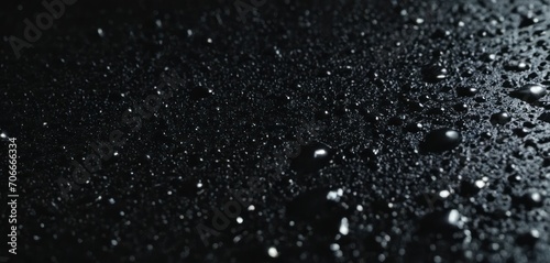  a black and white photo of water droplets on a black surface with a light reflection in the middle of the image.