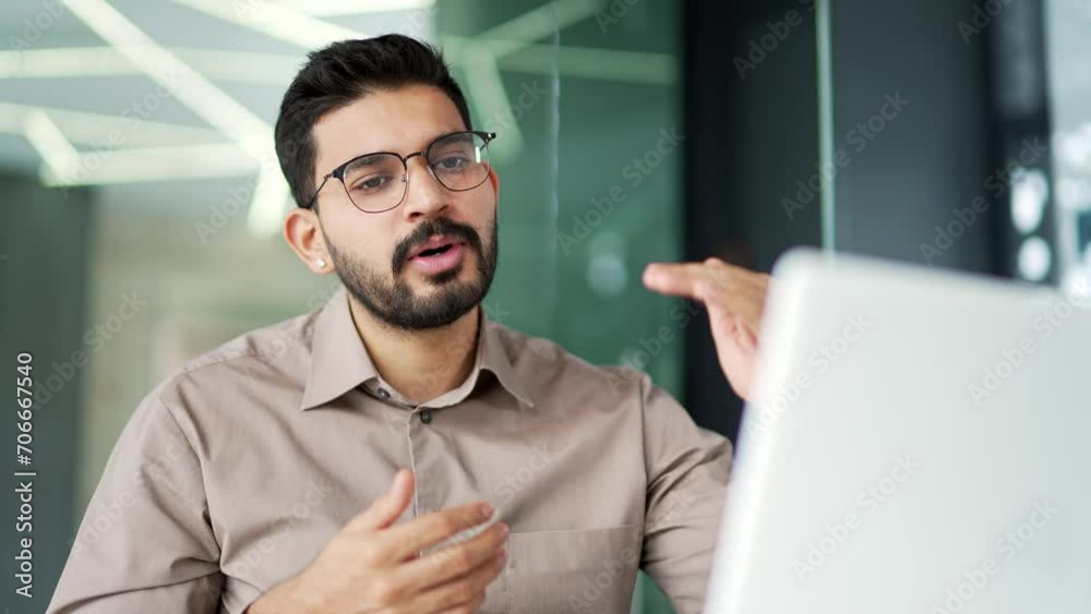 Confident businessman talking on a video call using a laptop sitting at workplace in business office. A male coach speaks remotely, has a conversation at an online conference or on a webinar. Close up
