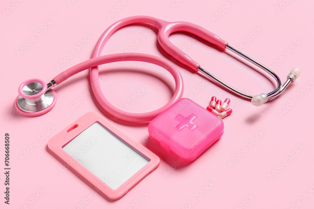 Stethoscope, pills organizer and badge on pink background
