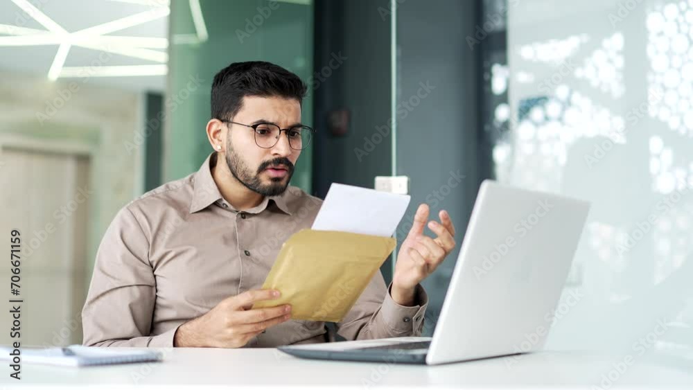 Disappointed bearded businessman in a shirt reading letter with bad news sitting at workplace in business office. Worried upset male employee in glasses frustrated by received unpleasant notification Disappointed bearded businessman in a shirt reading letter with bad news sitting at workplace in business office. Worried upset male employee in glasses frustrated by received unpleasant notification