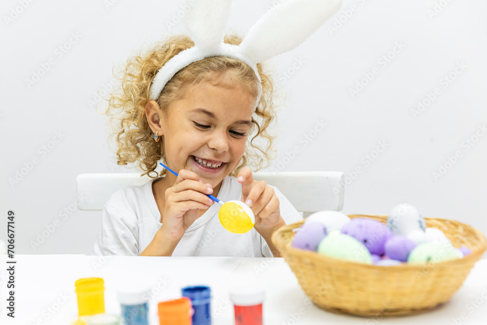 child painting Easter eggs on white background. Little girl in bunny ears dye colorful egg for Easter hunt. Home decoration with flowers, basket and rabbit for spring holiday celebration. child painting Easter eggs on white background. Little girl in bunny ears dye colorful egg for Easter hunt. Home decoration with flowers, basket and rabbit for spring holiday celebration.