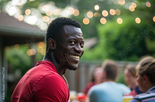 A man standing with a smile in a red shirt by a table of people © olegganko