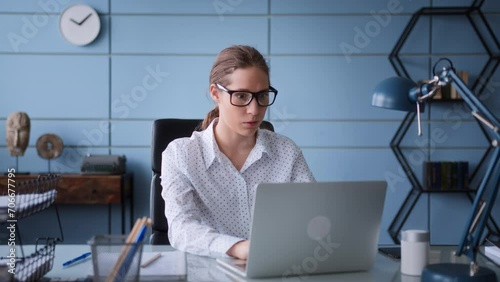 young woman in white shirt and eyeglasses sit at table desk in office, working at laptop. frustrated and worried, frowns, gives up and closes computer to have a break and breath out.