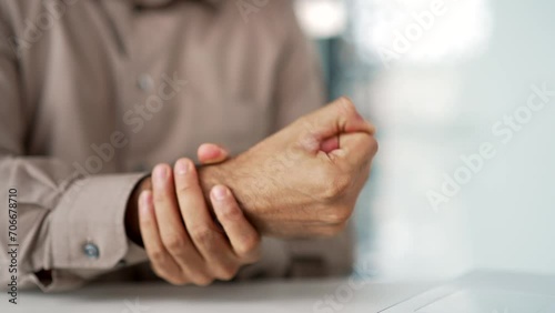 Close up of a man's hand massaging his wrist while sitting at a workplace at a desk in a business office. A male employee suffers from joint pain, has an injury, rubs a sore muscle, does an exercise photo
