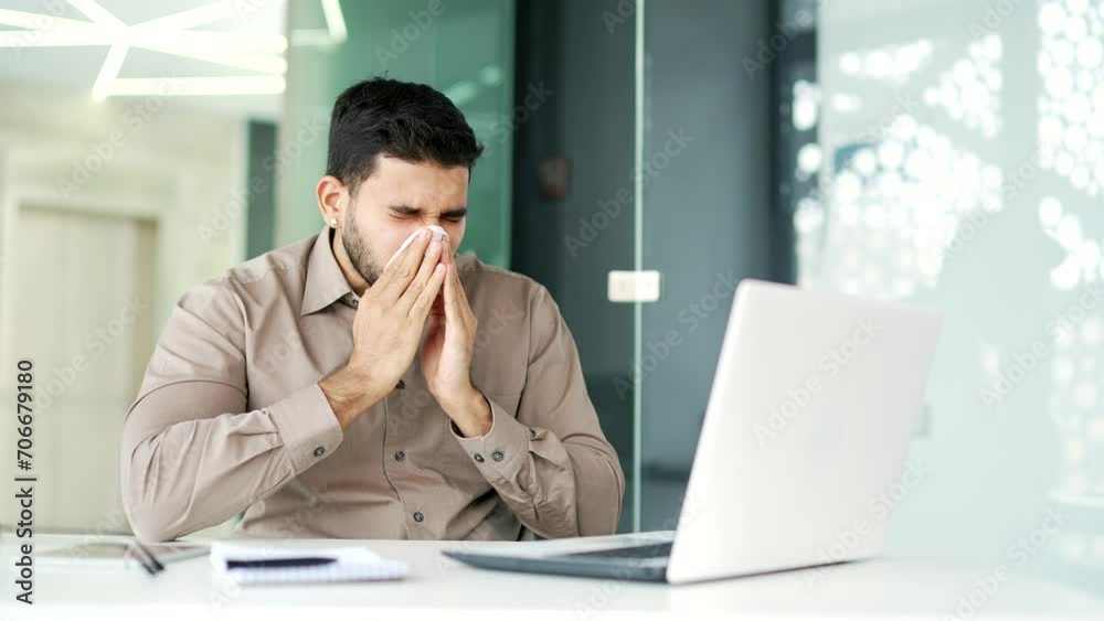 Sick businessman suffers from a runny nose while working on a laptop sitting at a workplace in a business office. Upset male wipes his nose with a handkerchief. A bearded man has a cold, virus or flu Sick businessman suffers from a runny nose while working on a laptop sitting at a workplace in a business office. Upset male wipes his nose with a handkerchief. A bearded man has a cold, virus or flu