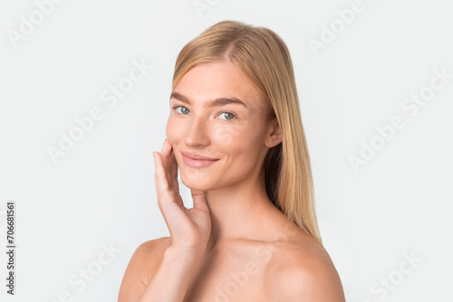 Pretty blonde lady gently applies moisturizer to smooth skin  portrait