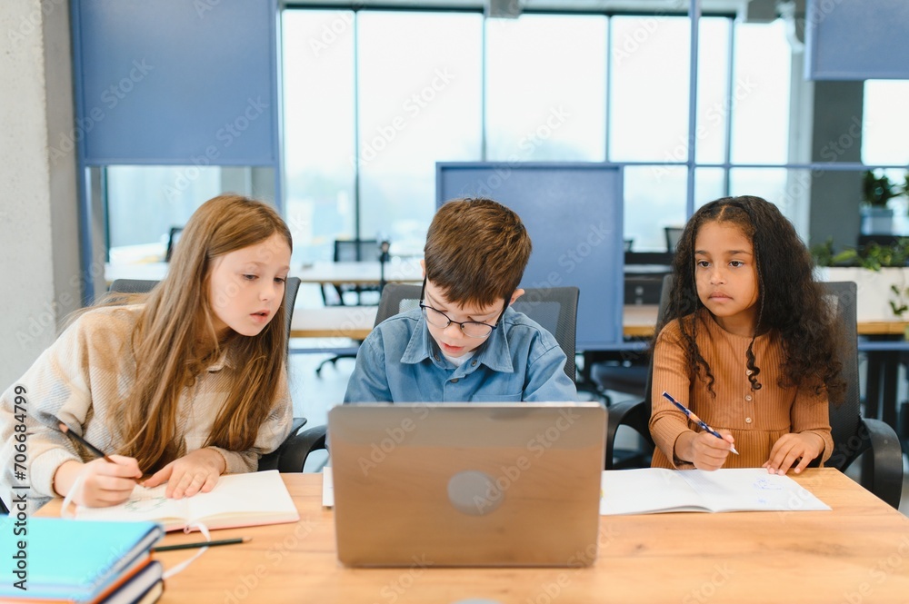 Obraz premium Portrait of smart schoolgirls and schoolboys looking at the laptop in classroom