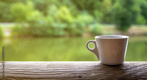A cup of coffee on a wooden table against the background of a blurred lake. The concept of vacation and travel.