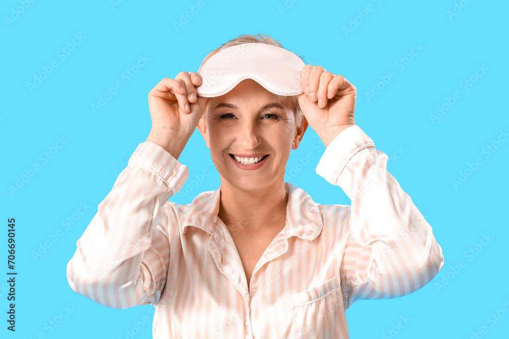 Mature woman in pajamas with sleeping mask on blue background Mature woman in pajamas with sleeping mask on blue background