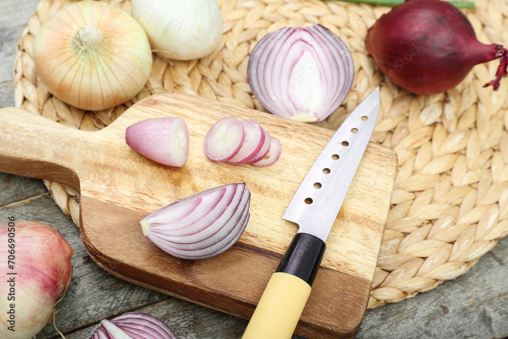 Board and wicker mat with different kinds of onion on brown wooden background