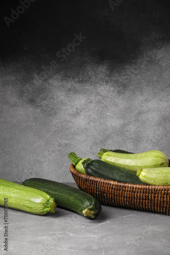 Wicker bowl with fresh zucchini on grey background