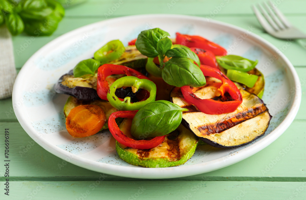 Plate with grilled vegetables and basil on green wooden table Plate with grilled vegetables and basil on green wooden table