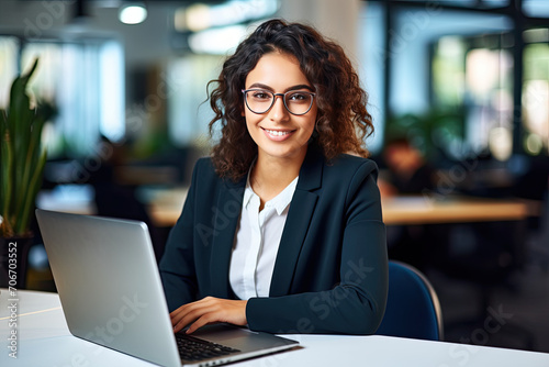 Cheerful Young Latina Executive at Desk, Focused on Laptop Exploring Innovative Business AI Solutions