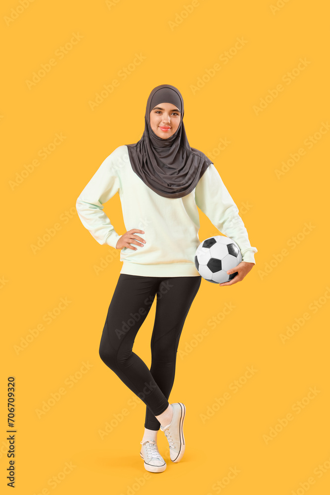 Fototapeta premium Young Muslim woman with soccer ball on yellow background