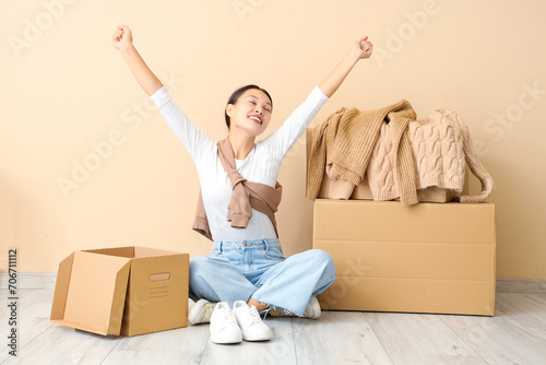 Happy young Asian woman with parcels near beige wall