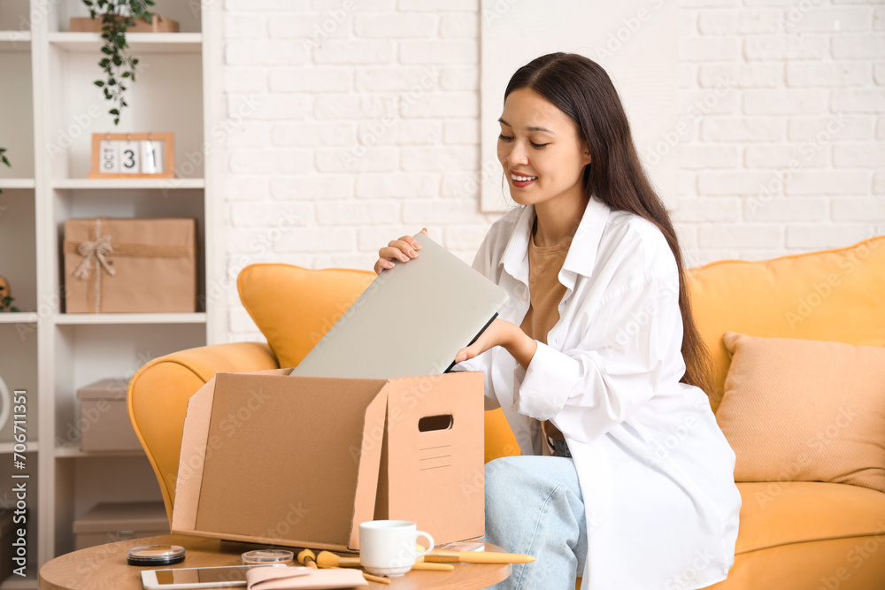 Young Asian woman taking new laptop from parcel at home Young Asian woman taking new laptop from parcel at home