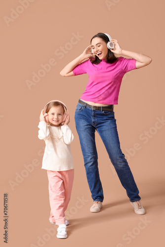 Beautiful mother with her cute little daughter in headphones listening music on brown background