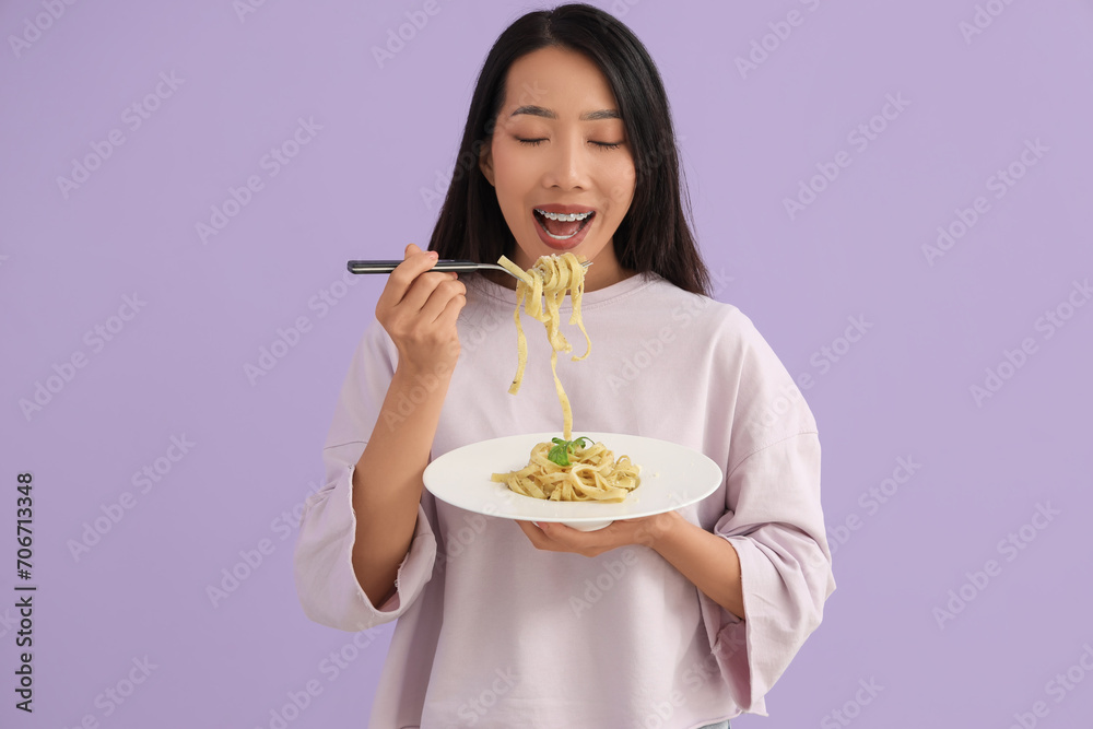 Young Asian woman eating tasty pasta on lilac background Young Asian woman eating tasty pasta on lilac background