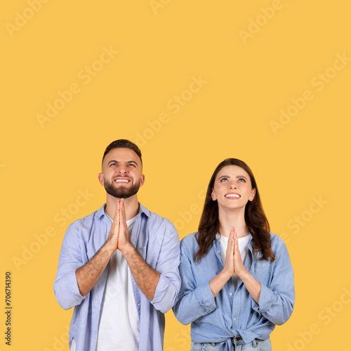 Hopeful couple with hands in prayer position, looking up at copy space