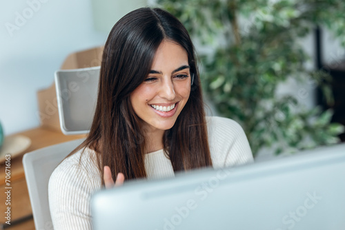 Business woman making video call with computer while talking with earphone sitting in modern office.