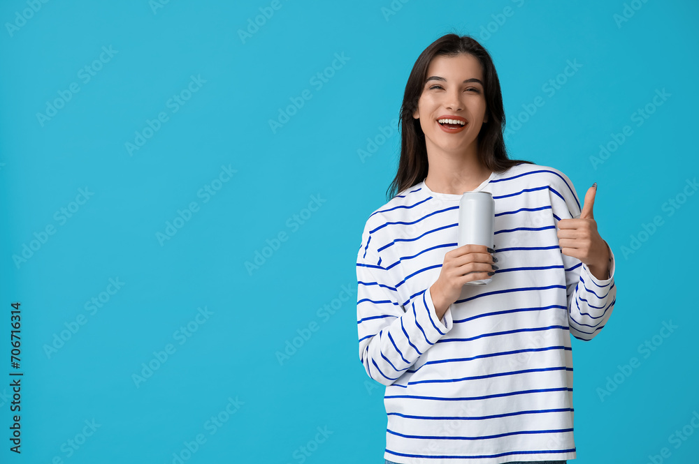 Beautiful young woman holding can of cold beer and showing thumb-up gesture on blue background Beautiful young woman holding can of cold beer and showing thumb-up gesture on blue background