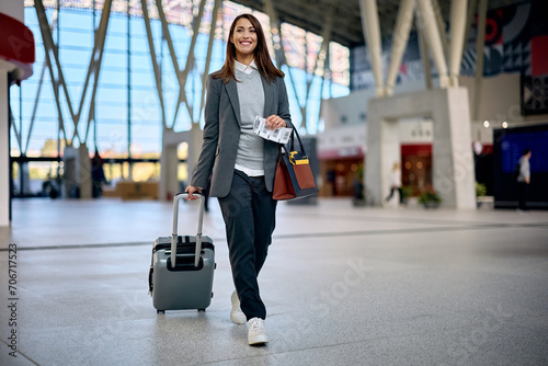 Happy businesswoman with carrying on suitcase walking at train station.